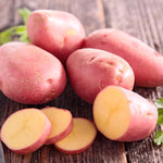 four whole pink potatoes and one sliced sitting on brown wood background