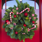 Candy Cane Christmas wreath made from fresh evergreen foliage, decorated with red and white candy canes, peppermint swirls, and shiny red baubles, hanging on a red door.