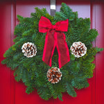 Classic Red Christmas Wreath Classic red Christmas wreath made from fresh evergreen foliage, decorated with three frosted pine cones and a red ribbon bow, hanging on a red door. 1