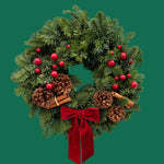 Festive Red Christmas Wreath Front view of the Festive Red wreath featuring evergreen foliage, glossy red berries, pinecones, and cinnamon sticks tied with a velvet bow, set against a plain green background. 3
