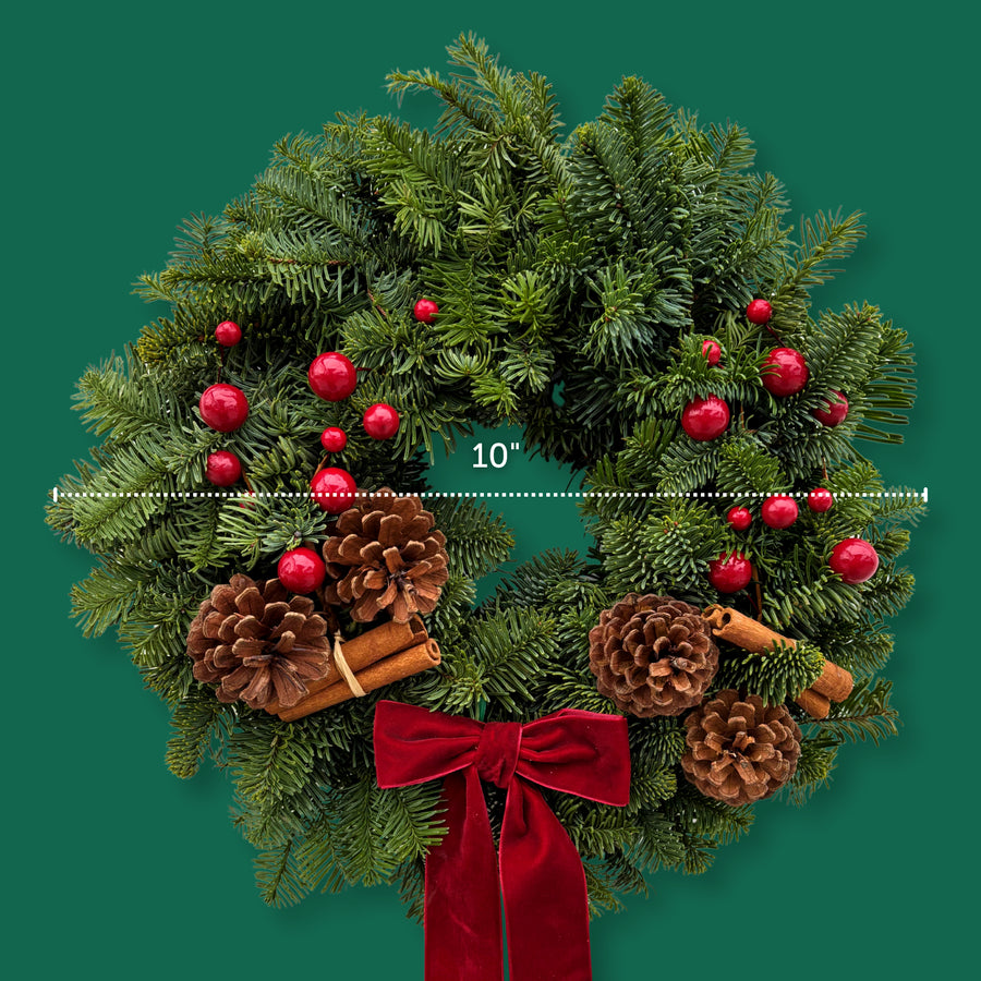 Festive Red Christmas Wreath The Festive Red Christmas wreath shown on a green background with a measurement line indicating a 10-inch diameter, decorated with pinecones, red berries, cinnamon sticks, and red velvet ribbon. 4