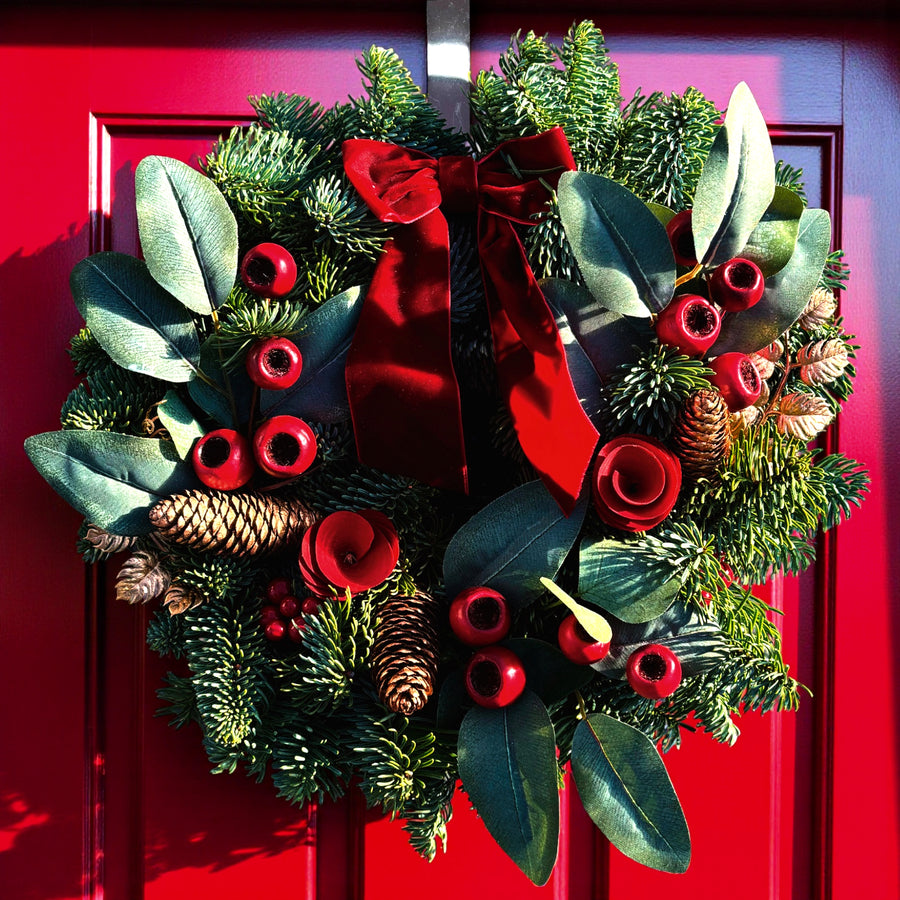 Red Rose and Rosehip Christmas Wreath A 10-inch festive wreath made from mixed evergreen foliage, pinecones, faux red berries, and velvet red roses, finished with a red ribbon bow and hung on a bright red front door. 1