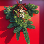 Star Christmas Swag Fresh evergreen door swag decorated with pinecones, red berries and wooden star ornaments, finished with a deep red ribbon bow, hanging on a red front door. 1