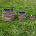 Mica Plant Pots - Dark Brown Cane Trio of dark brown rattan-look plant pots with black inner linings, arranged on natural grass. 2