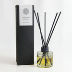 Freckleface Peony & Vanilla 125ml Reed Diffuser Peony and Vanilla reed diffuser with black reeds in a clear glass bottle filled with golden liquid, placed beside its tall black box with white label. 1