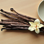 Freckleface Peony & Vanilla 125ml Reed Diffuser Vanilla pods arranged on a light background beside a pale vanilla flower with cream petals and brown centre. 3