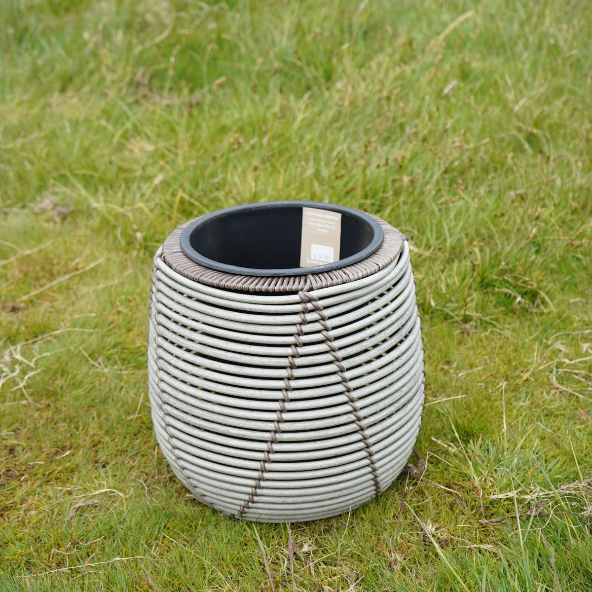Mica Plant Pots - White Cane Medium-sized white faux-rattan plant pot with label, shown outdoors on grass. 4
